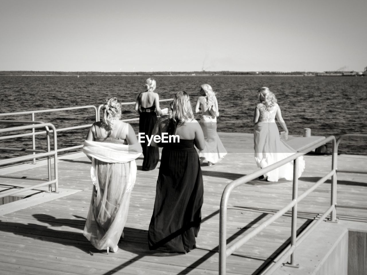 Rear view of female friends walking on pier over sea against clear sky