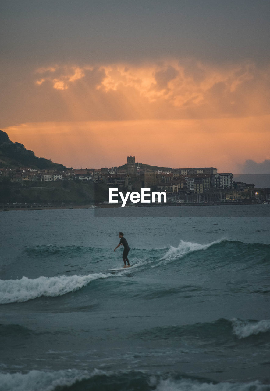 Man surfing on sea against sky during sunset