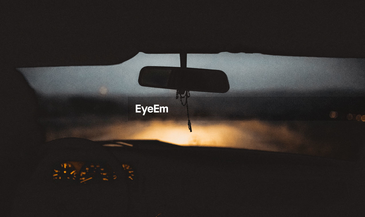 Silhouette rear-view mirror against windshield in car during sunset