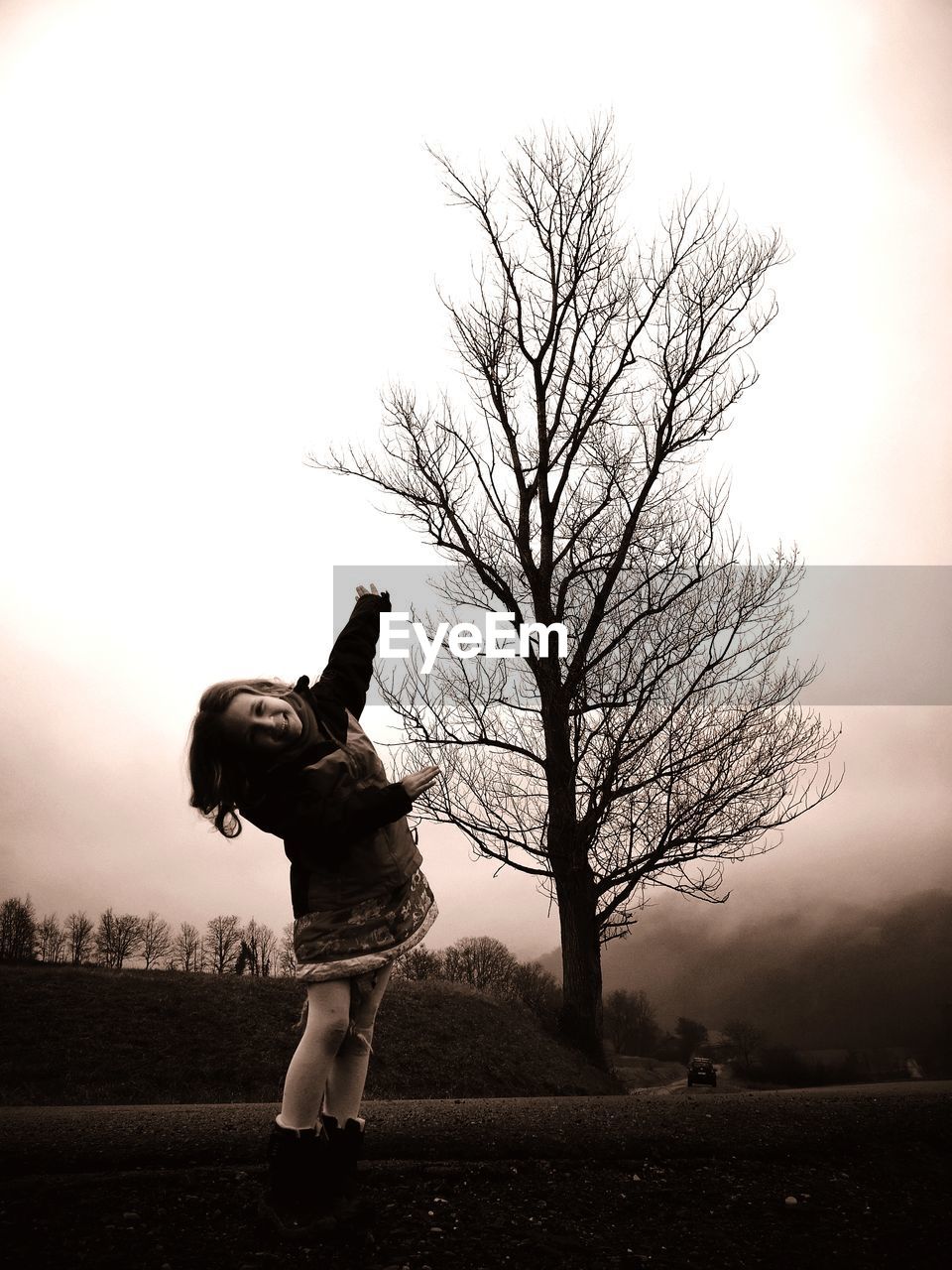 Girl standing by bare tree on field against sky