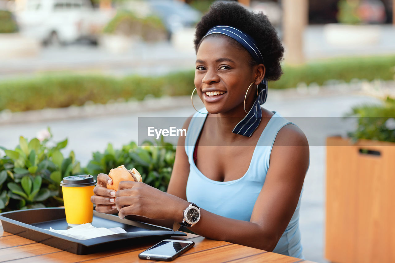 Cute african woman having lunch outdoors in city cafe. an african-american woman smiles