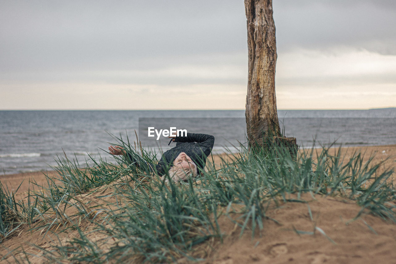 Young woman exercising while lying down by tree trunk at beach