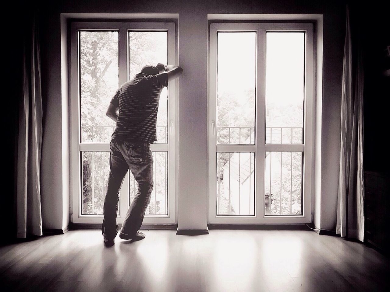 Full length rear view of man standing against window at home