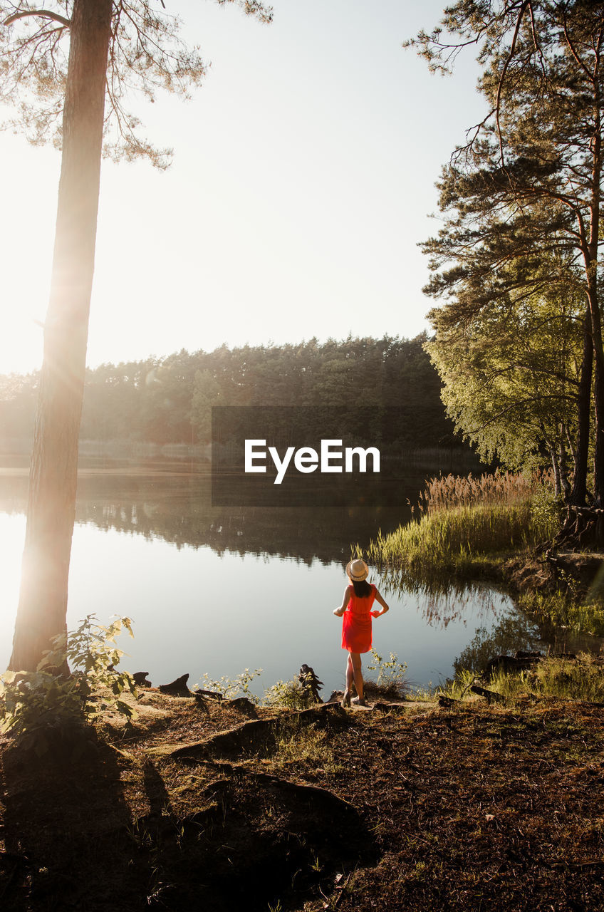 Rear view of woman standing by lake against sky