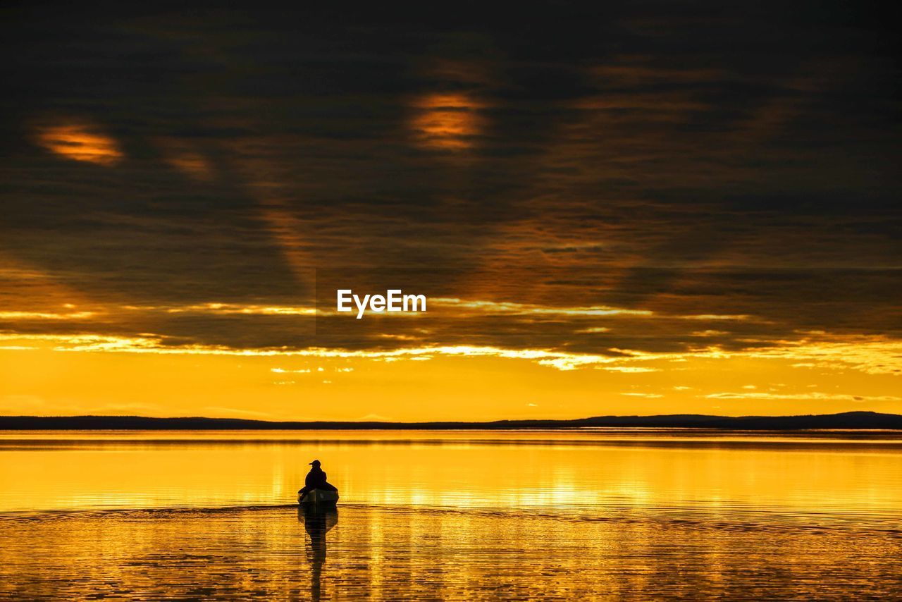 Silhouette person sailing canoe in river against cloudy sky during sunset