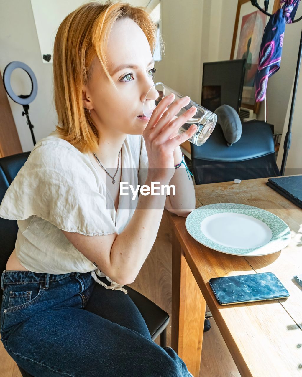 one person, women, adult, sitting, indoors, young adult, casual clothing, food and drink, lifestyles, person, blond hair, clothing, female, table, portrait, drink, hairstyle, food, cup, furniture, home interior, domestic room, coffee, three quarter length, looking, domestic life, mug, technology, leisure activity