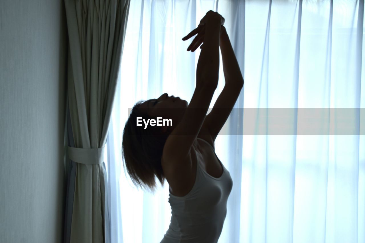 Close-up of woman dancing against curtain at home