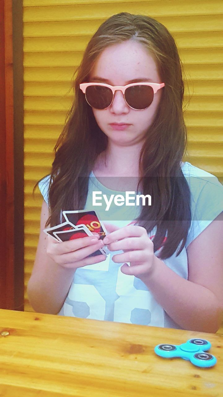 PORTRAIT OF A YOUNG WOMAN WEARING SUNGLASSES WHILE HOLDING SMART PHONE