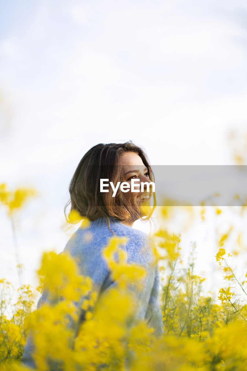 Woman standing by yellow flowers on field