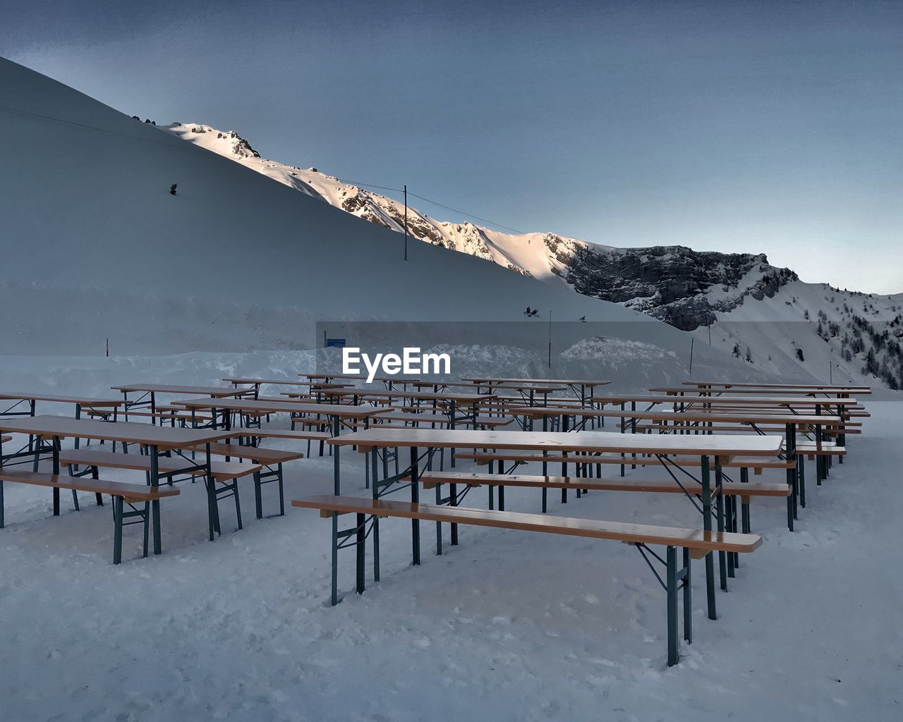 Empty tables and seats on snowcapped mountain against clear blue sky