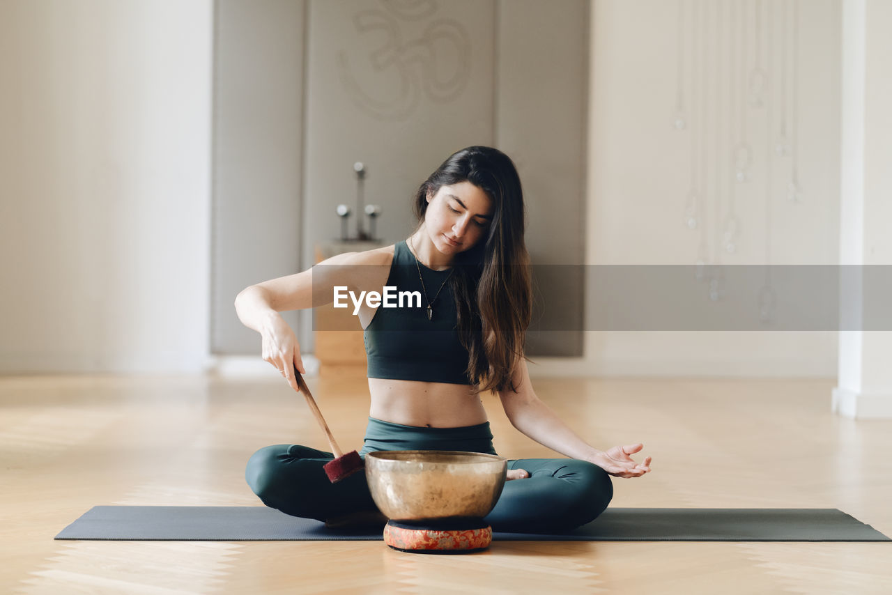 Woman playing rin gong while sitting on exercise mat 