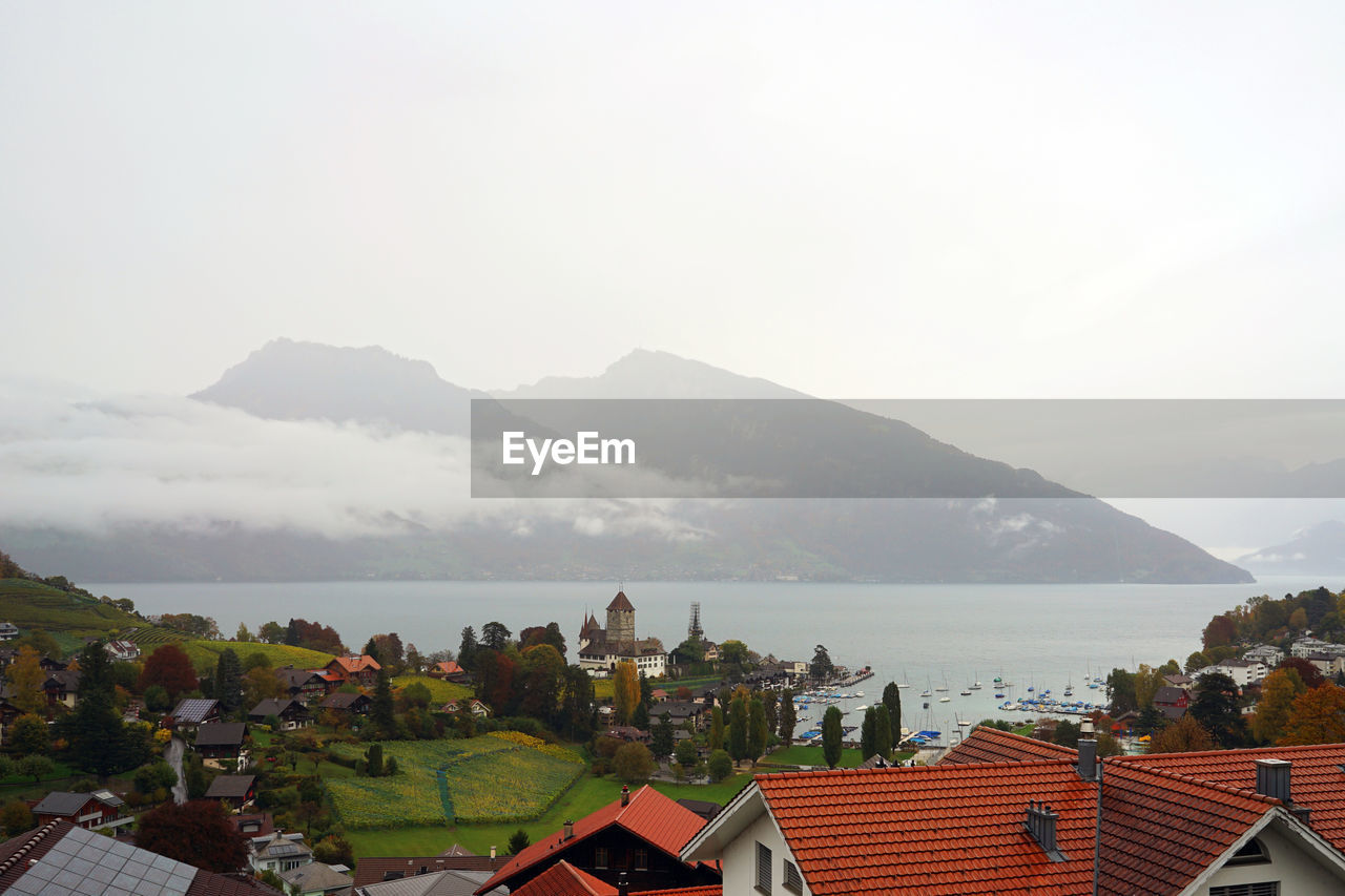 HIGH ANGLE VIEW OF HOUSES BY TOWN AGAINST SKY