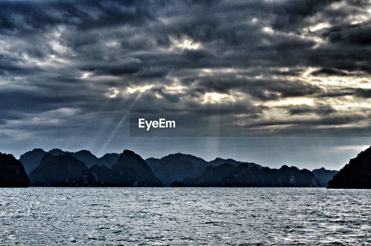 Scenic view of sea against mountains against cloudy sky