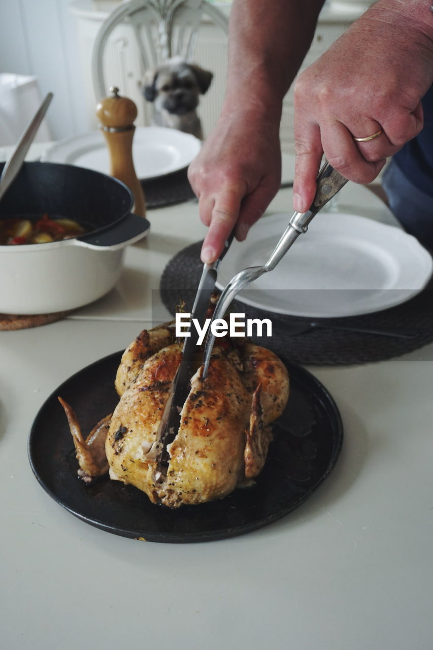 Cropped hand of woman cutting roasted chicken in plate