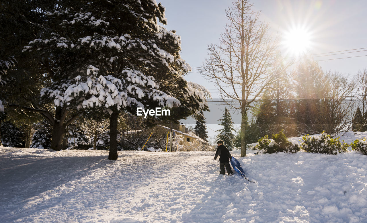 Boy with toboggan walking on snow during winter