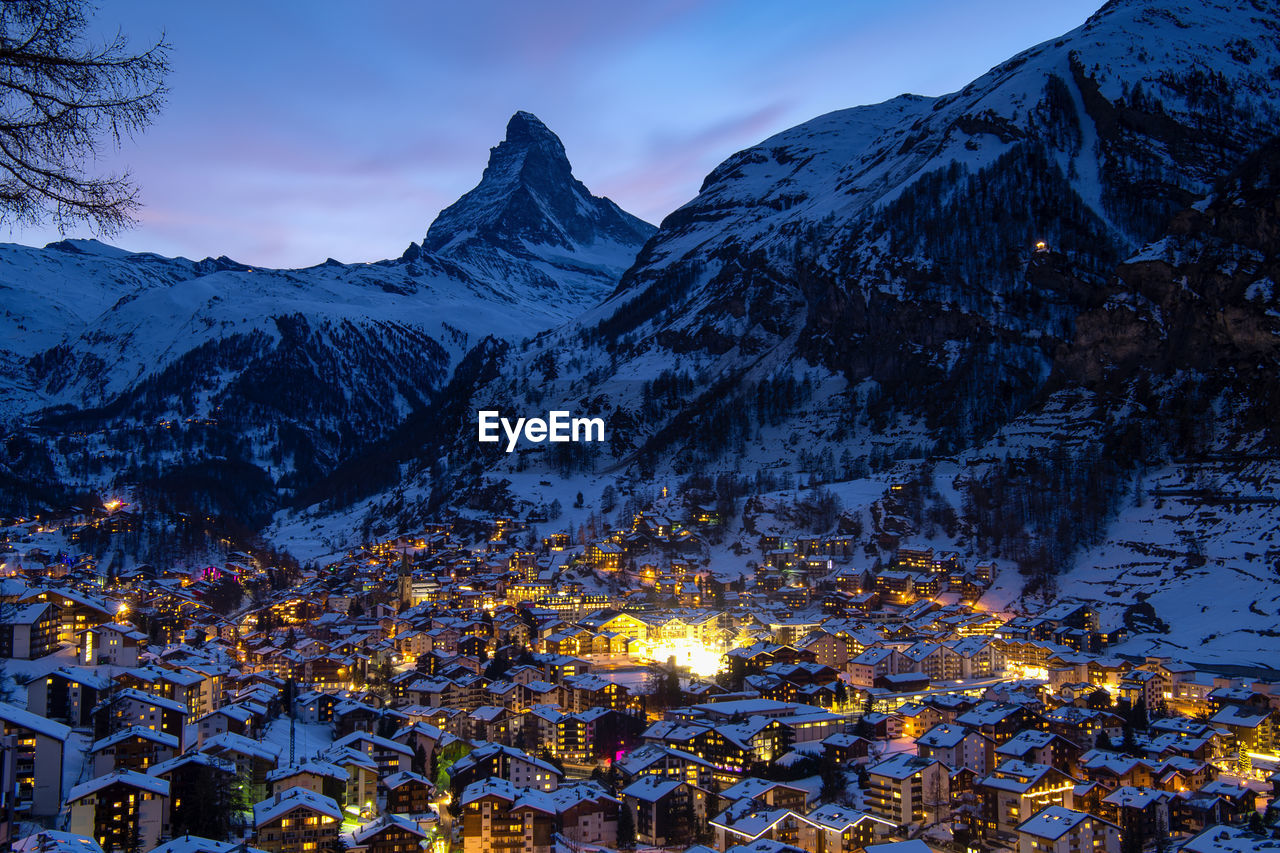 Buildings by snowcapped mountain in town at dusk