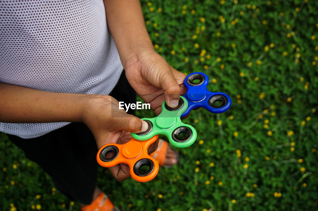 Low section of man holding colorful fidget spinners on grassy field