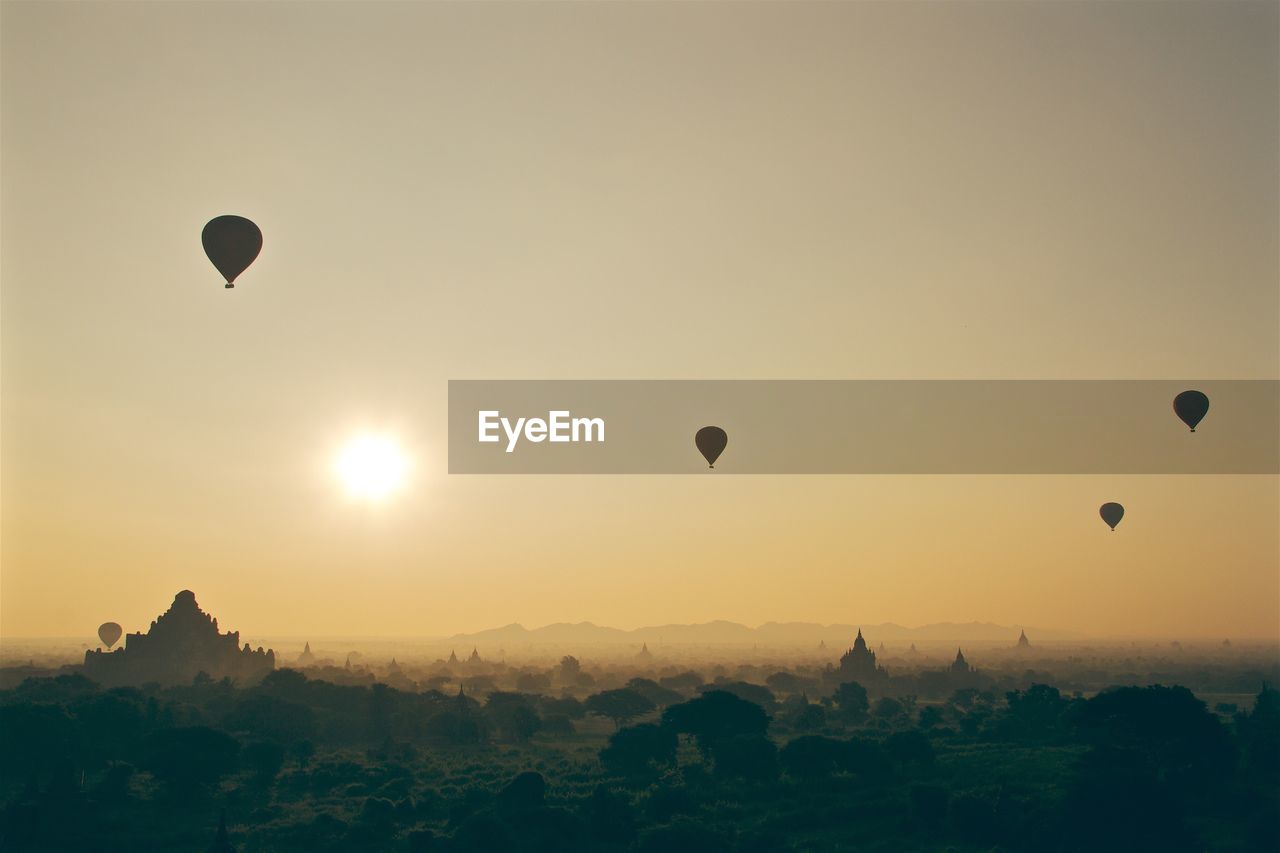 Hot air balloons over temples in city against clear sky during sunset