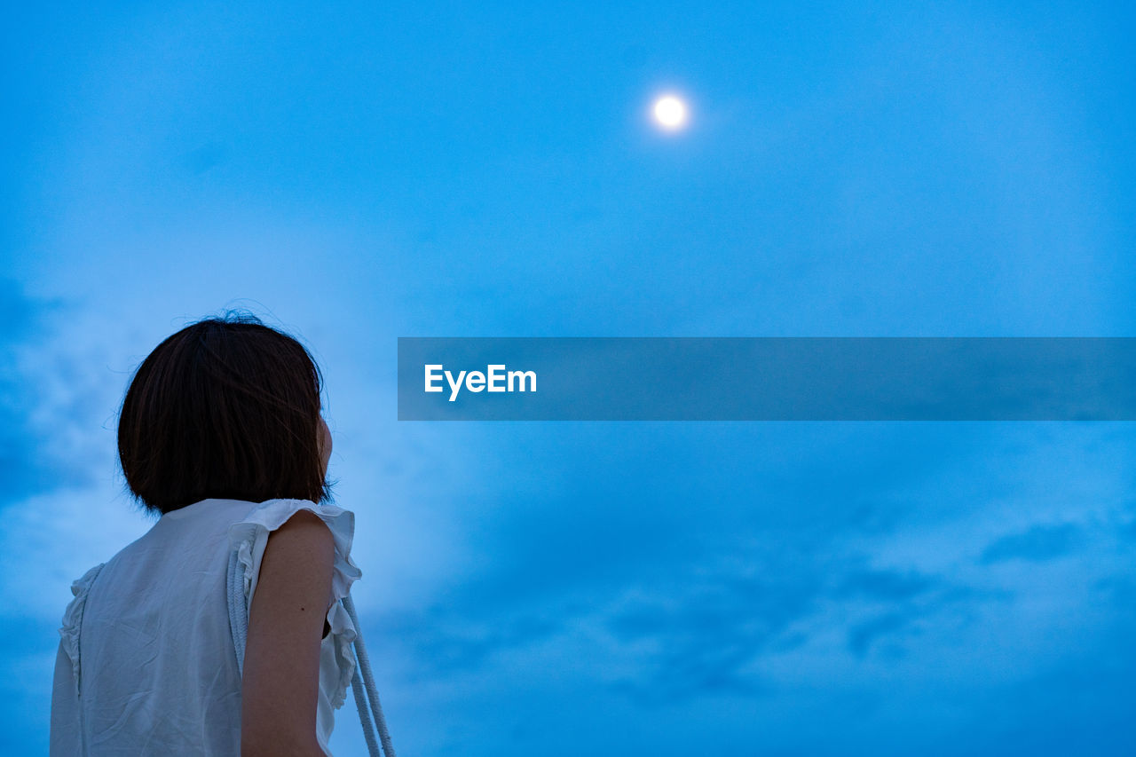 Low angle view of woman looking at moon in blue sky