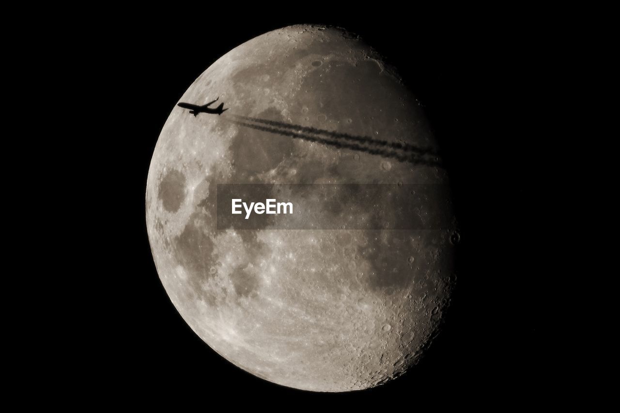 Airplane flying against moon at night