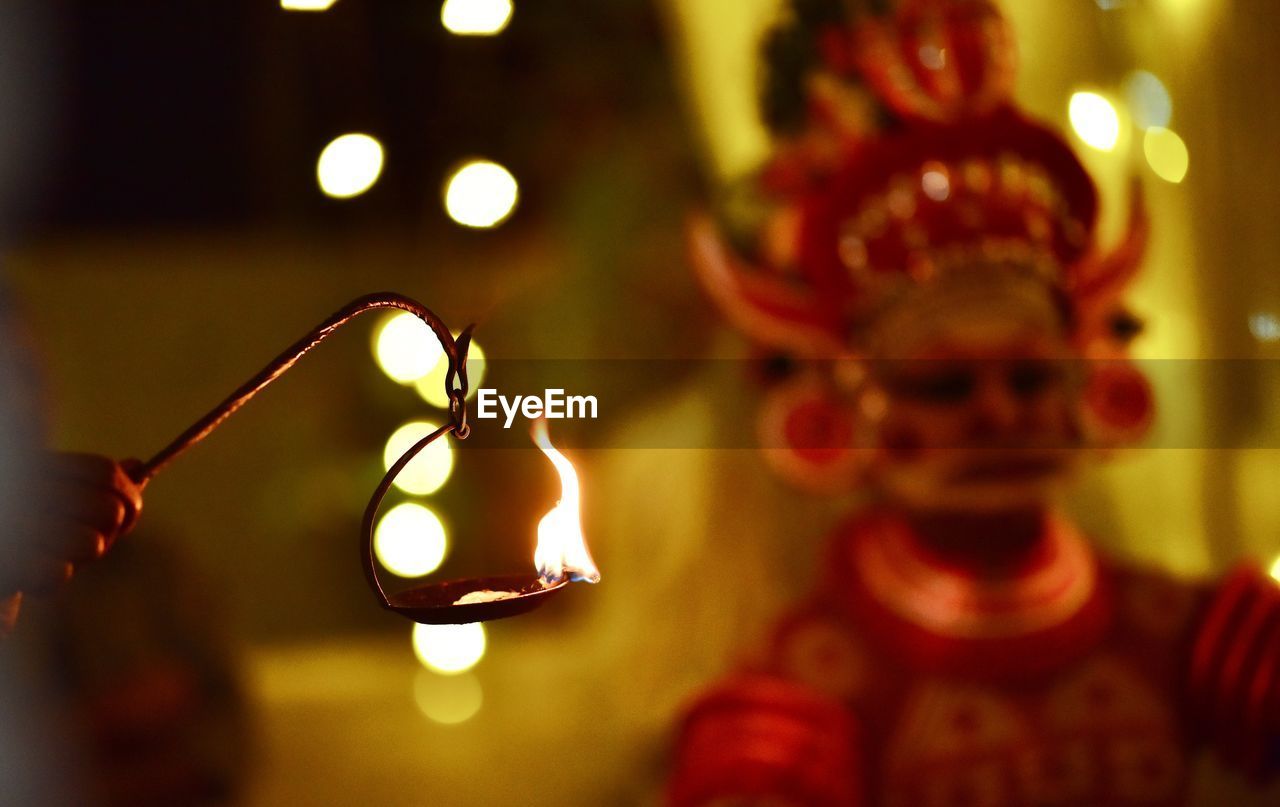 Cropped hand holding oil lamp with man wearing costume during celebration