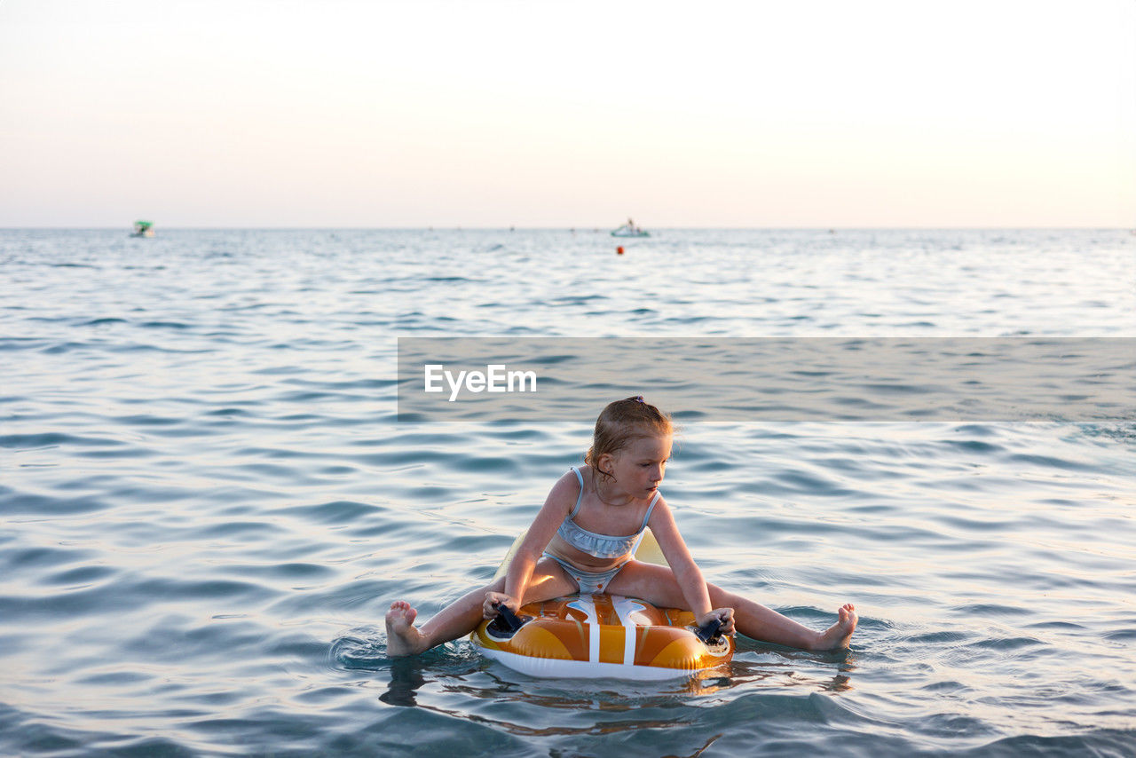 rear view of woman swimming in sea against sky during sunset