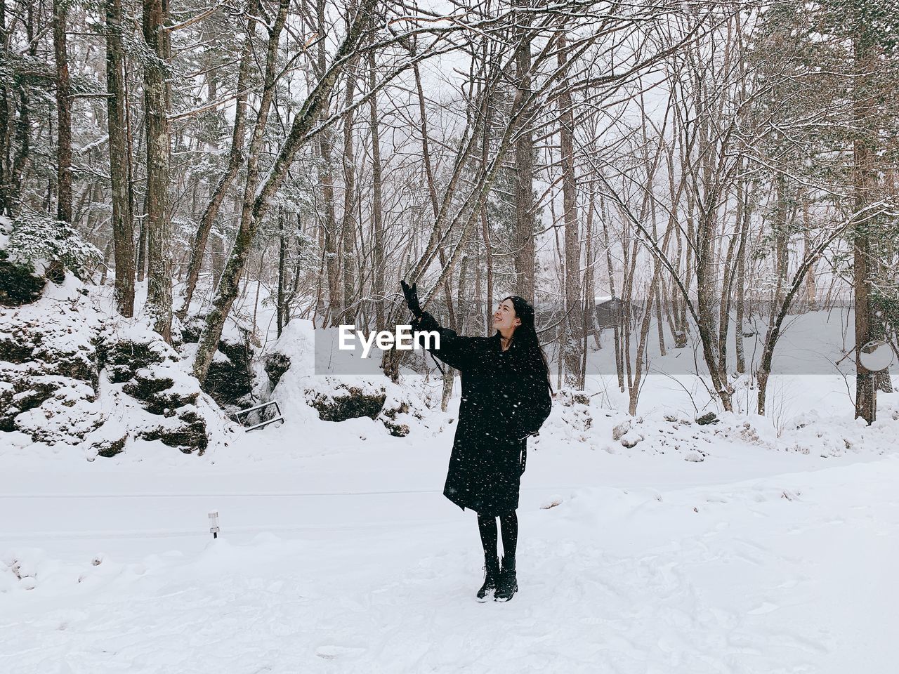 Full length of smiling mid adult woman standing on snow covered field