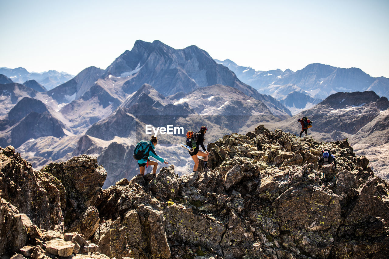 Group of mountaineers with backpacks climbing rough rocky mountain peak during summer adventure in pyrenees