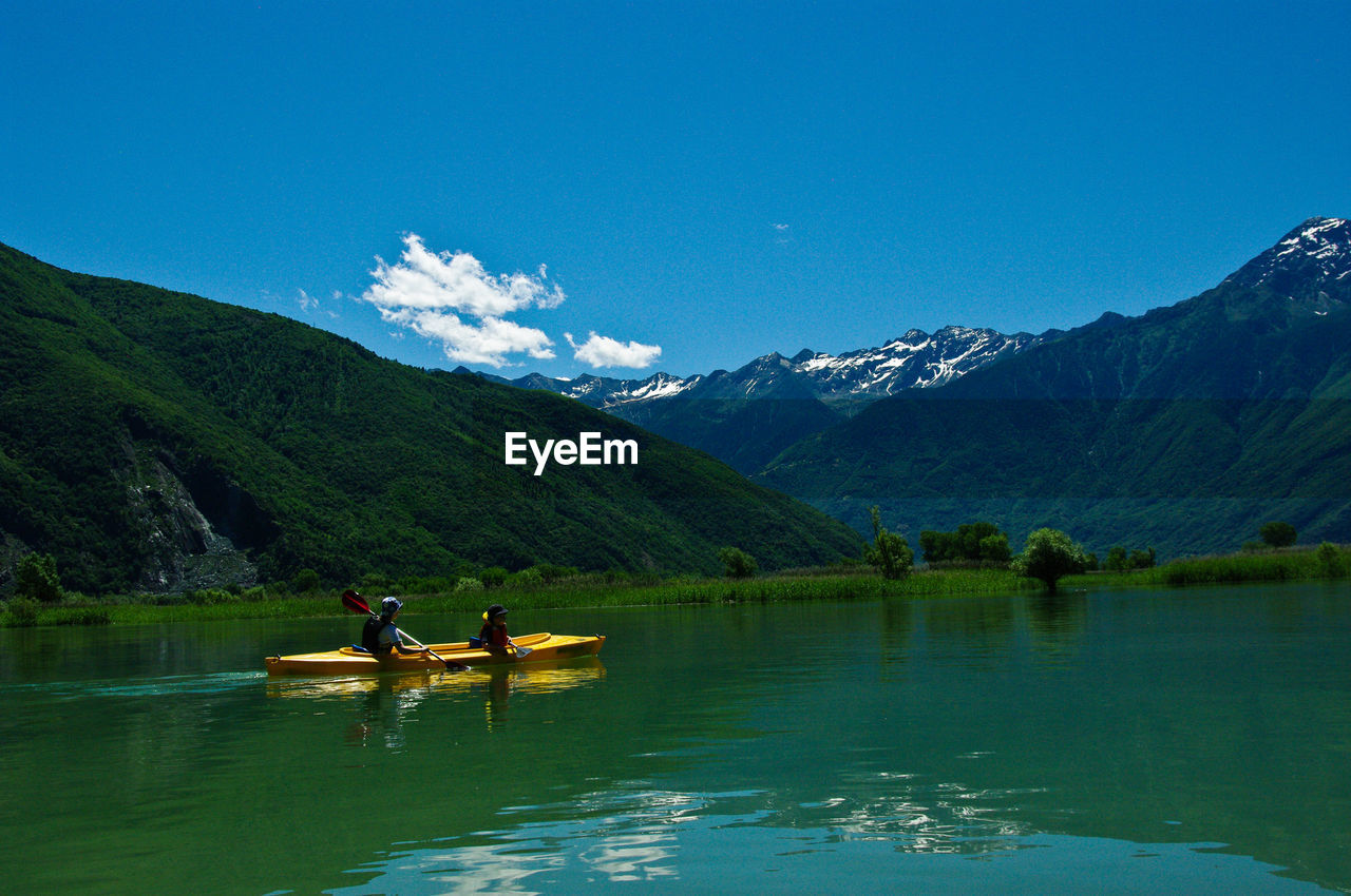People boating on lake against mountains