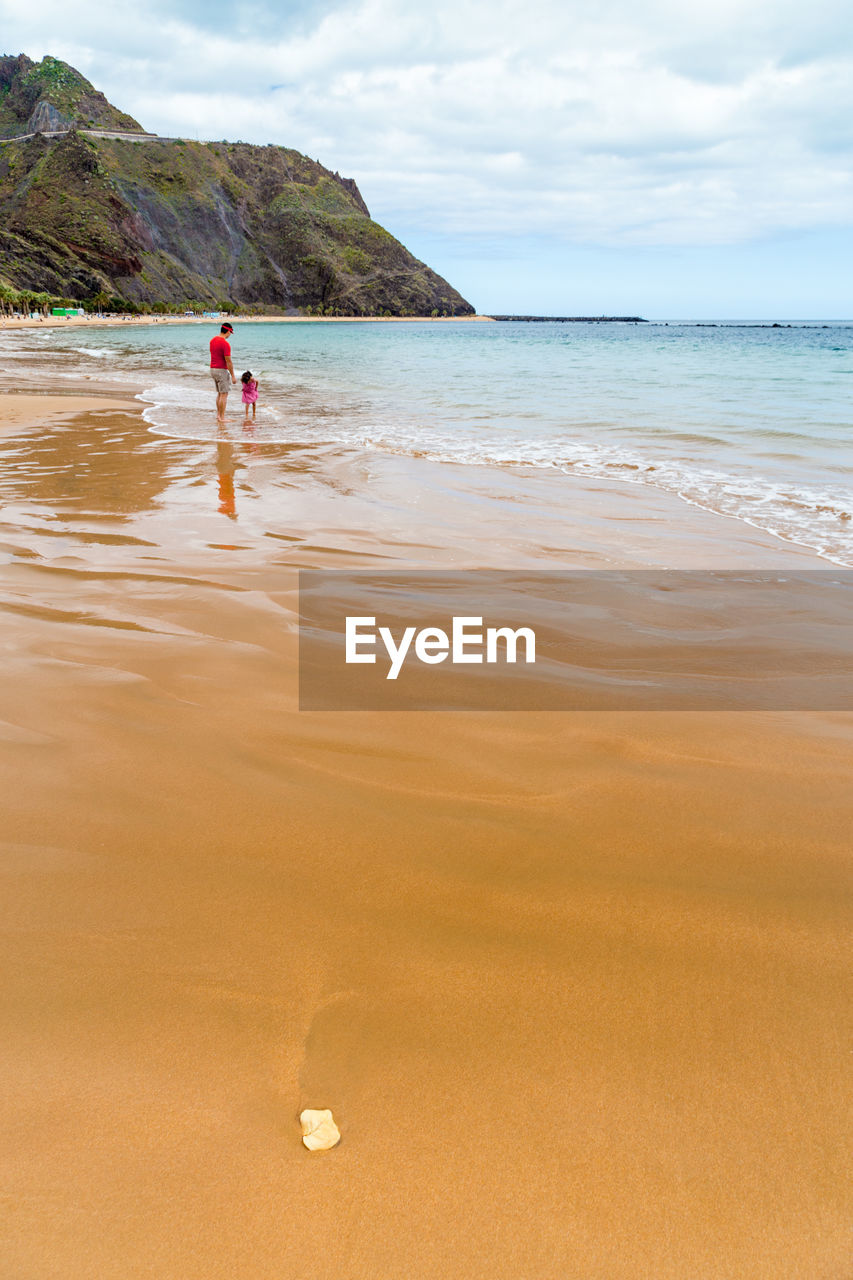 Father and daughter enjoying on wet shore against sky