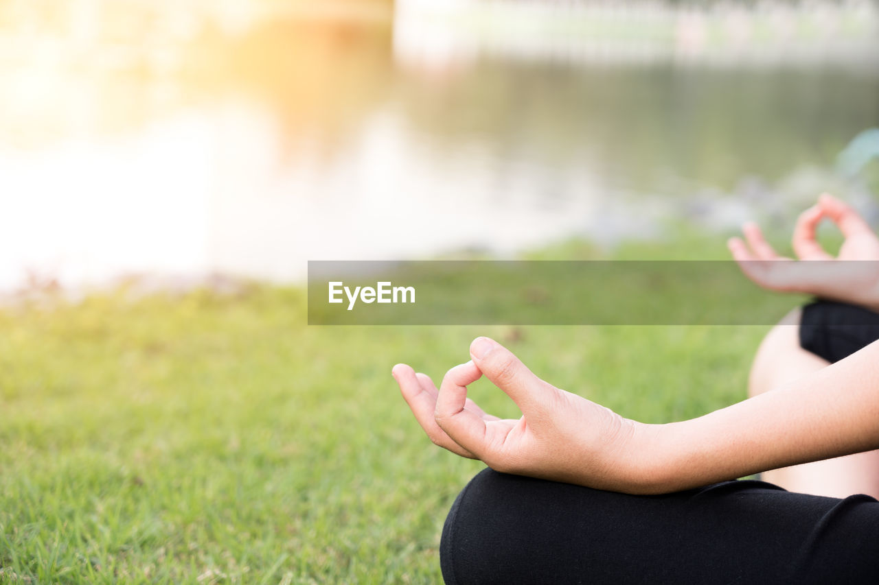 Cropped image of woman meditating at grassy lakeshore