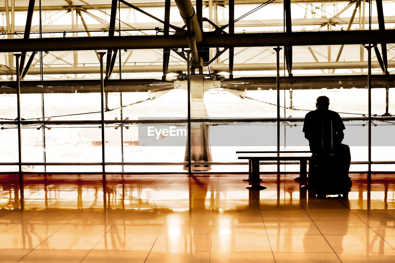 REAR VIEW OF SILHOUETTE MAN SITTING AT AIRPORT LOBBY