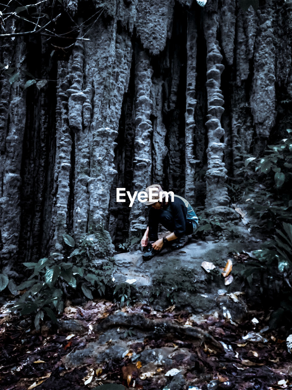 Full length of woman crouching on rock in forest