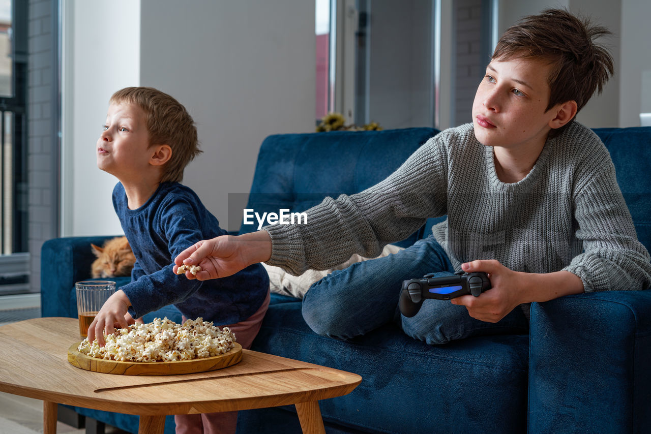 Two siblings boys sitting on a blue couch and playing video games. kids using technology