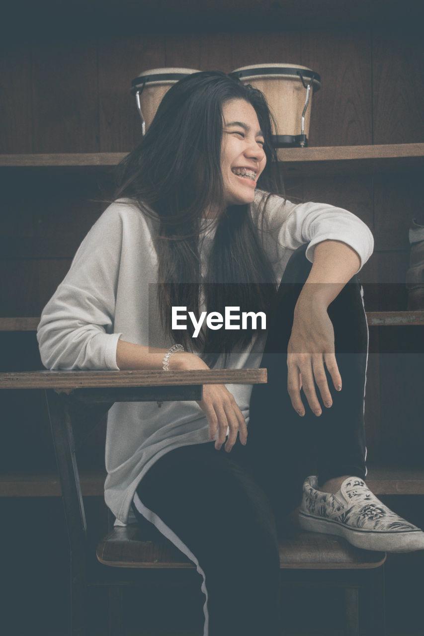 SMILING YOUNG WOMAN SITTING ON CHAIR IN ROOM