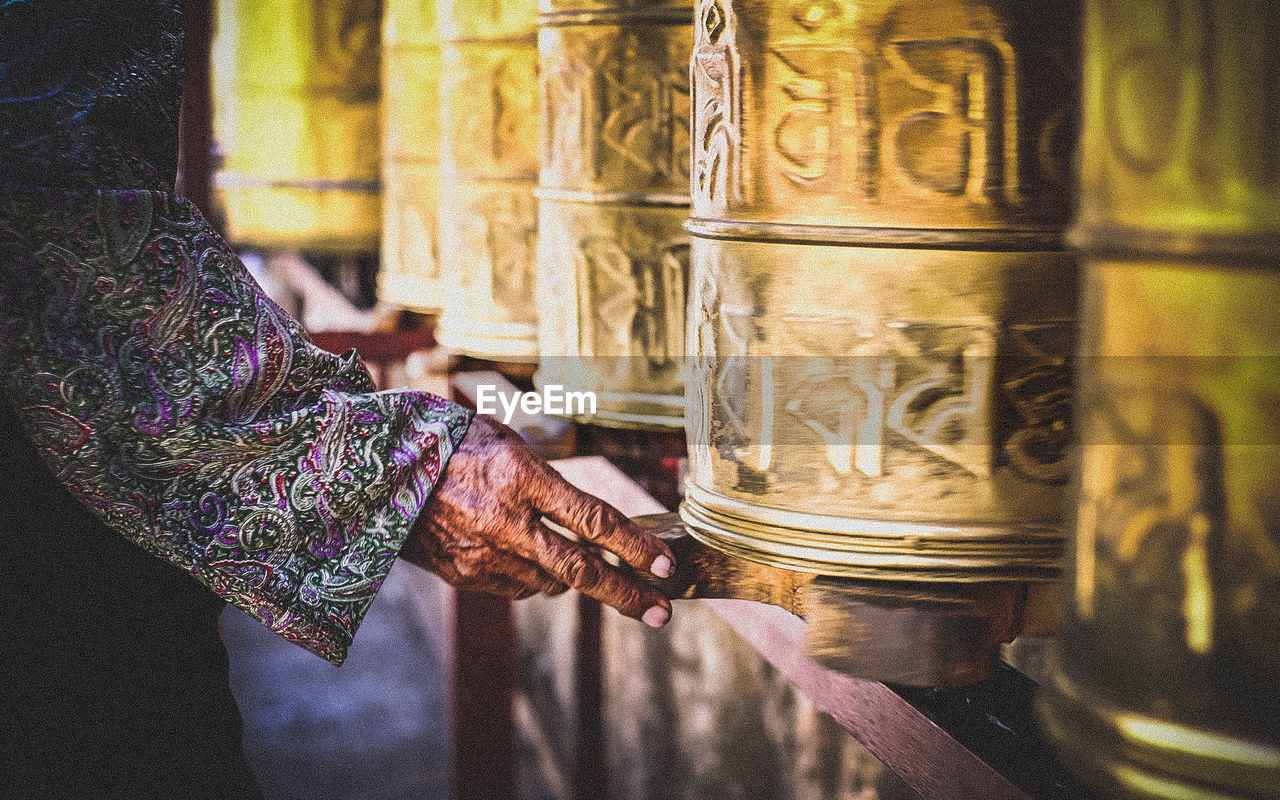 Cropped hand by prayer wheel at buddha temple