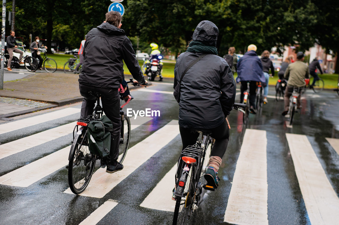 REAR VIEW OF PEOPLE BICYCLING ON ROAD IN CITY