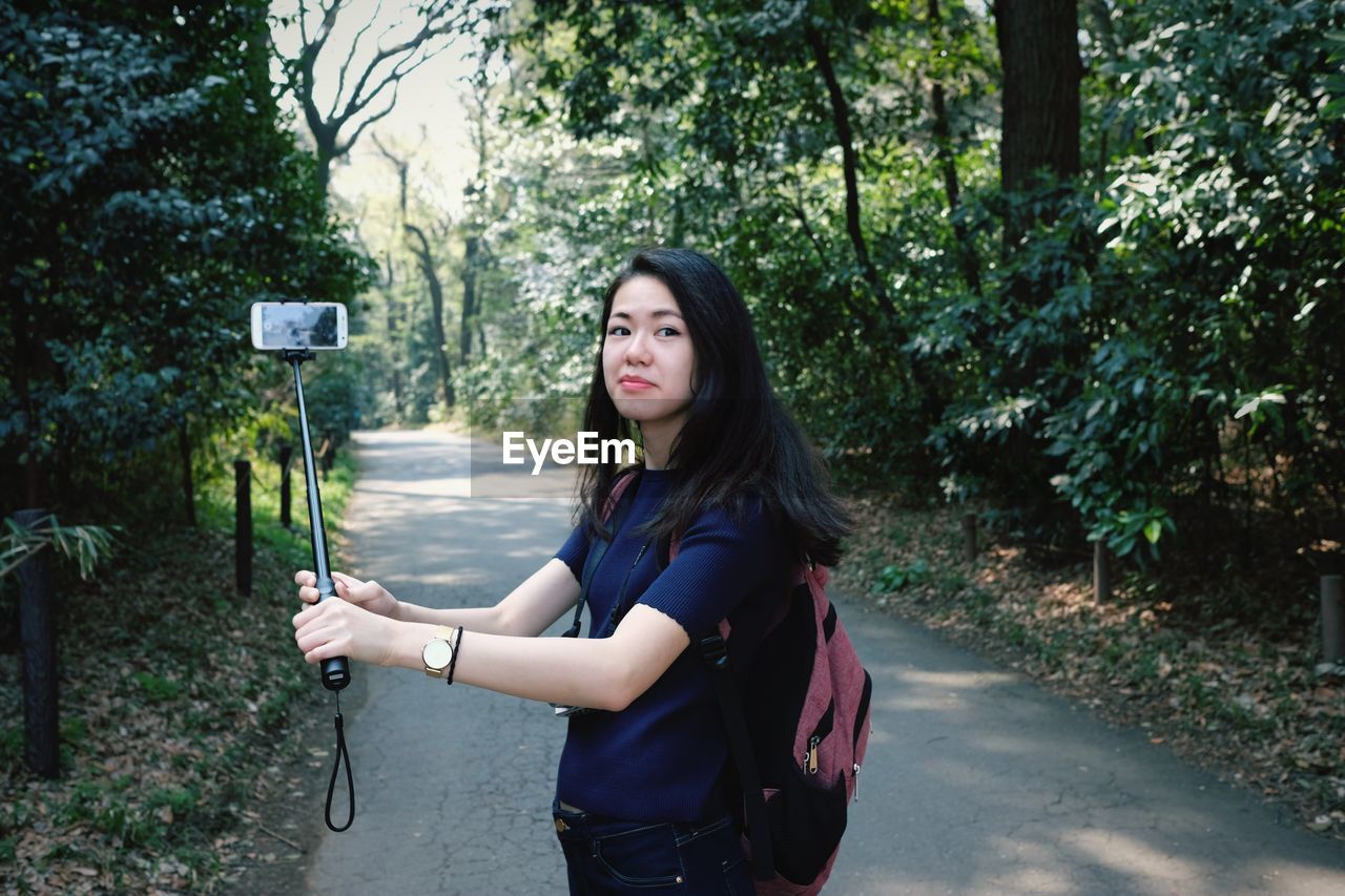 Portrait of beautiful woman standing by plants against trees