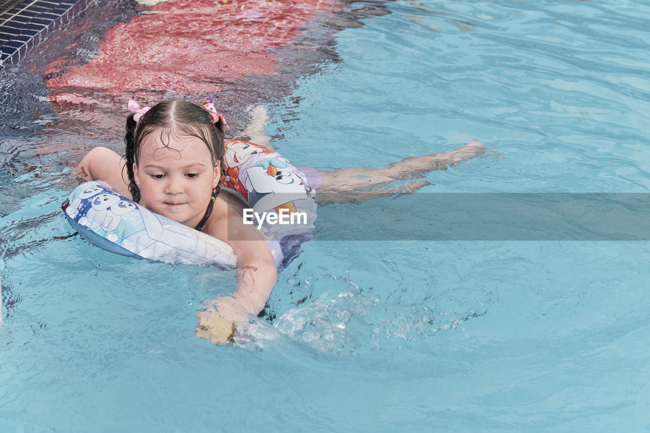 Happy adorable asian little girl swims in inflatable circle, having fun in open air thermal pool.