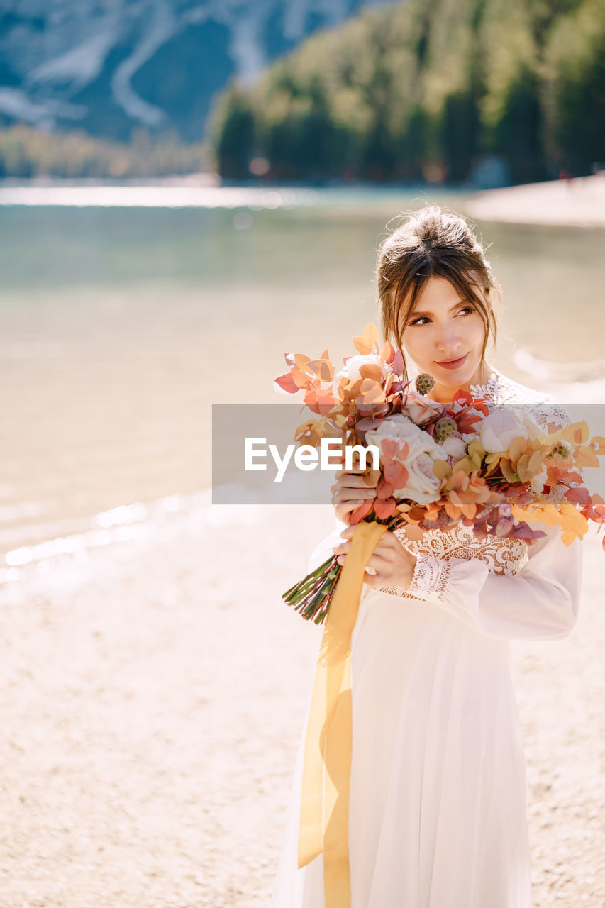 Bride holding bouquet looking away by riverbank