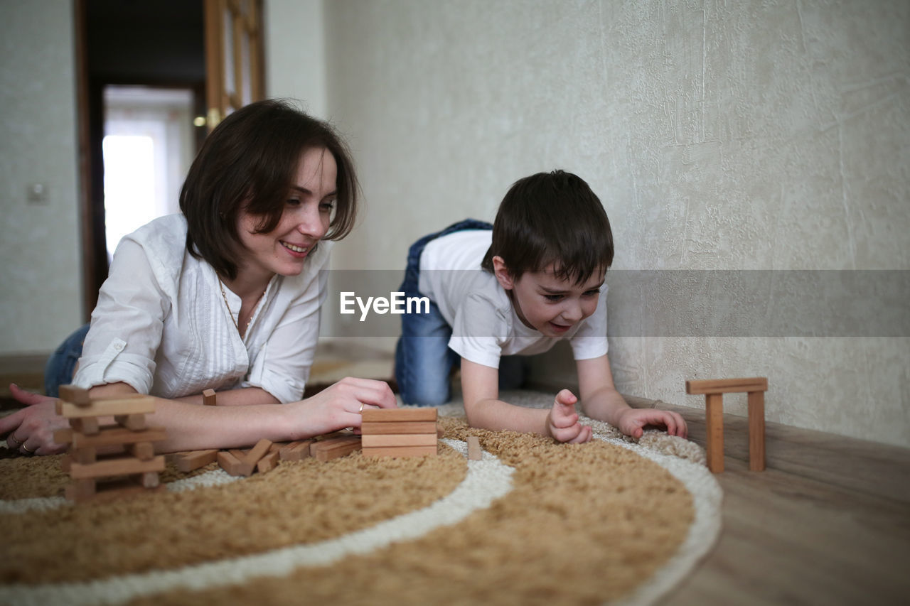 Happy family. mother and son playing in wooden designer and smiling. little boy having fun with 