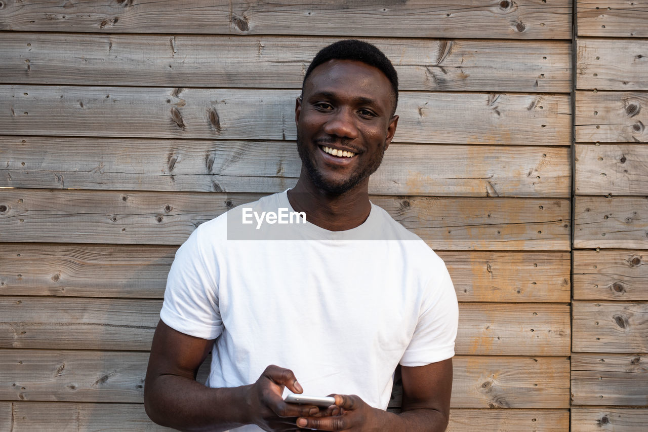 PORTRAIT OF SMILING YOUNG MAN STANDING AGAINST WALL