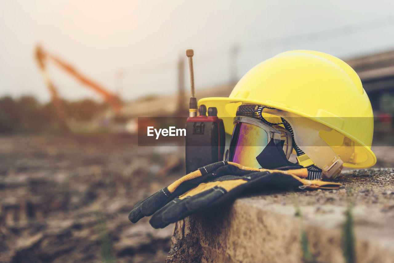 Close-up of yellow hardhat with walkie-talkie and gloves on retaining wall at construction site