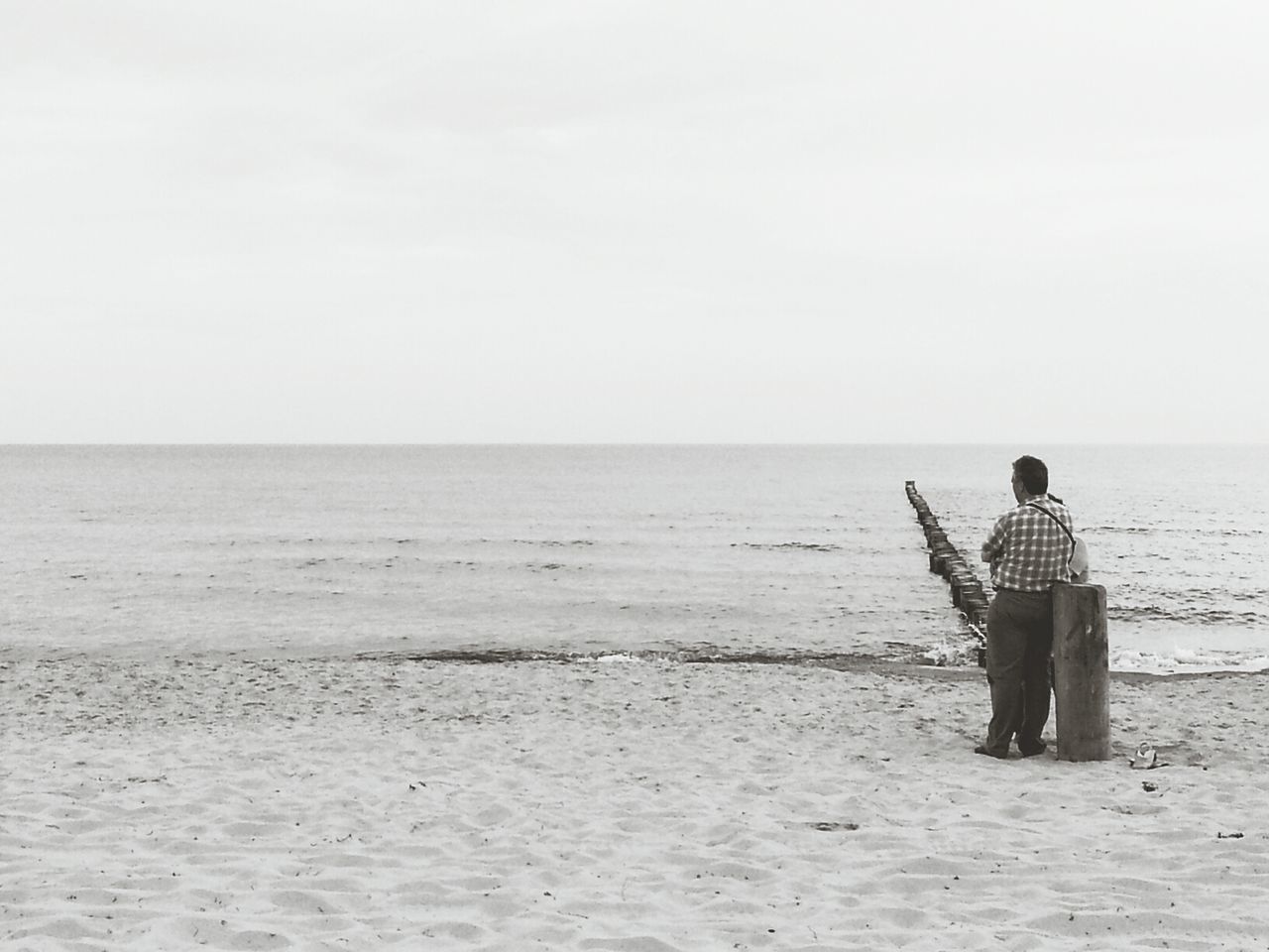 Rear view of man relaxing on wooden post at beach