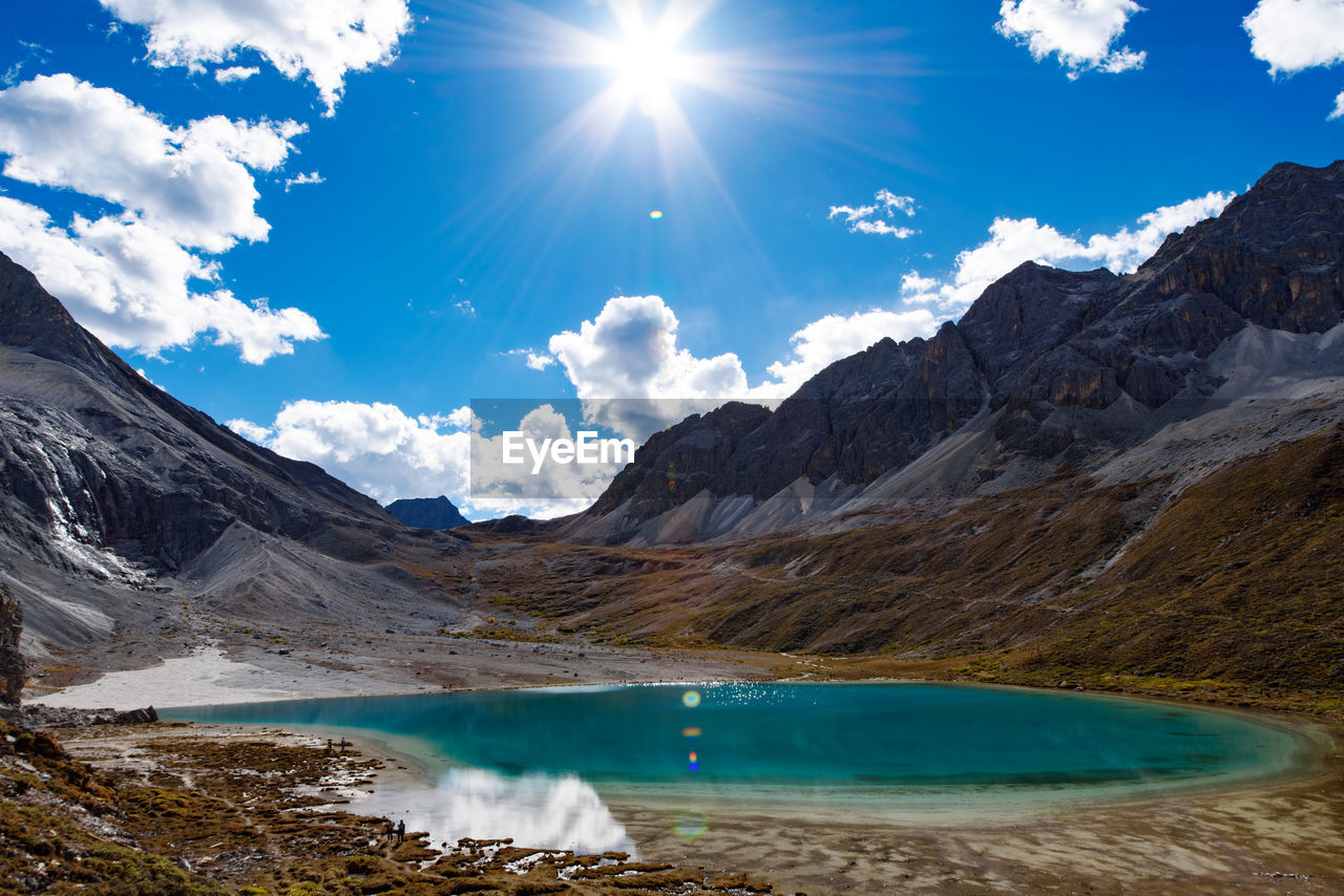 Scenic view of lagoon at mountains against blue sky on sunny day