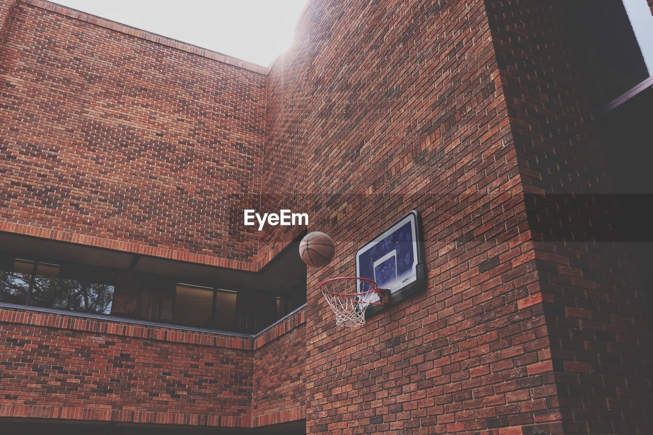 Low angle view of ball falling in basketball hoop attached on brick wall