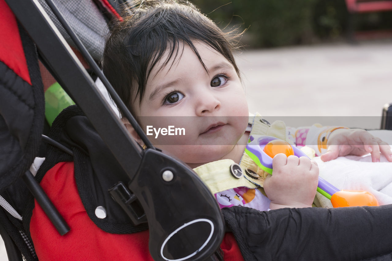 Portrait of cute baby girl with toy lying in stroller