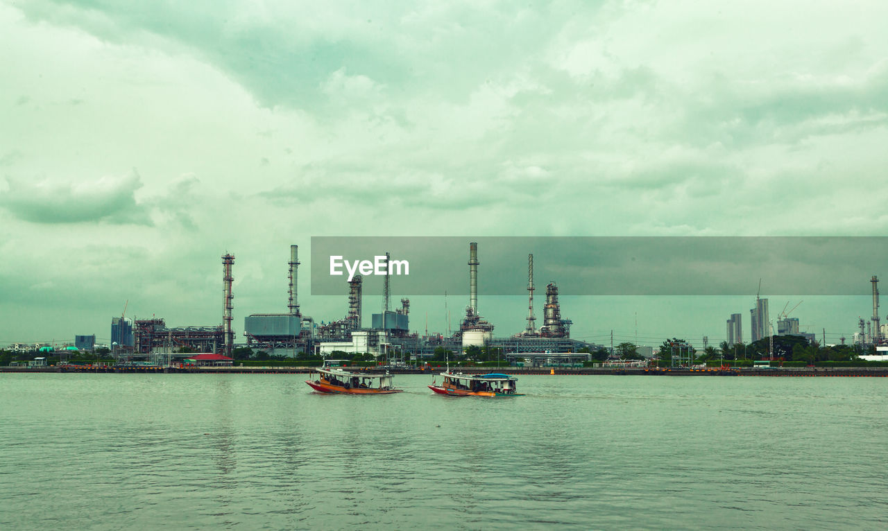 BOATS IN SEA BY FACTORY AGAINST SKY