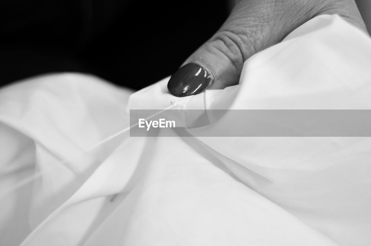 Cropped hand of woman sewing textile against black background