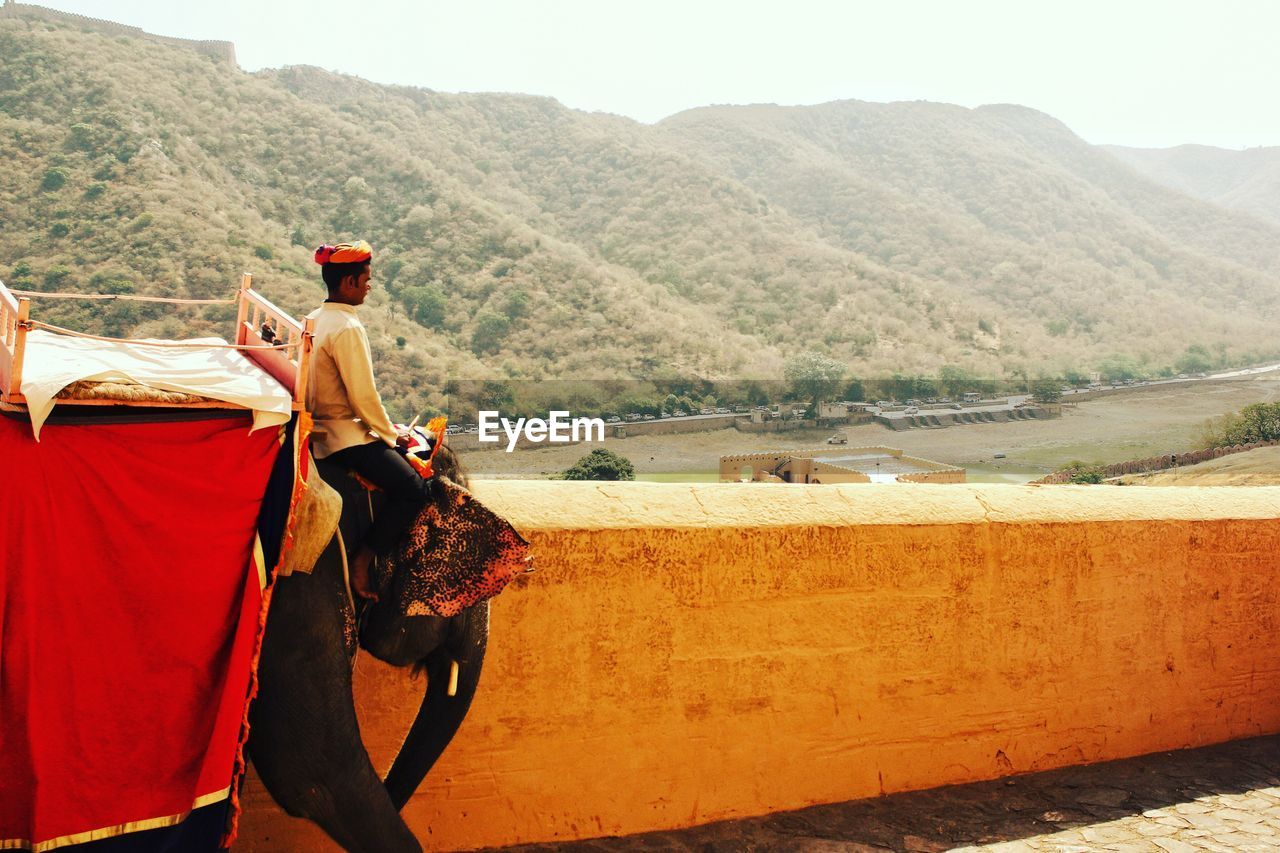 Man sitting on elephant against mountains